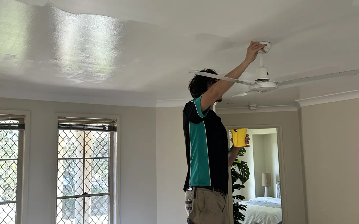 Tradesperson painting an interior ceiling with the room sheeted and protected