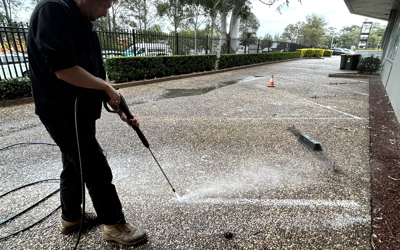 Operator using a pressure washing wand to clean line marking in a commercial car park